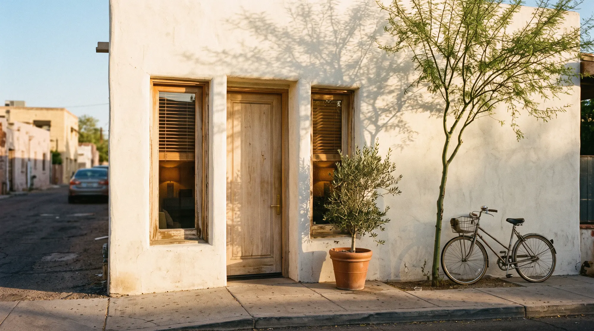 Solenne's white plaster front on Marshall Way, with an olive tree, a bicycle and late sun
